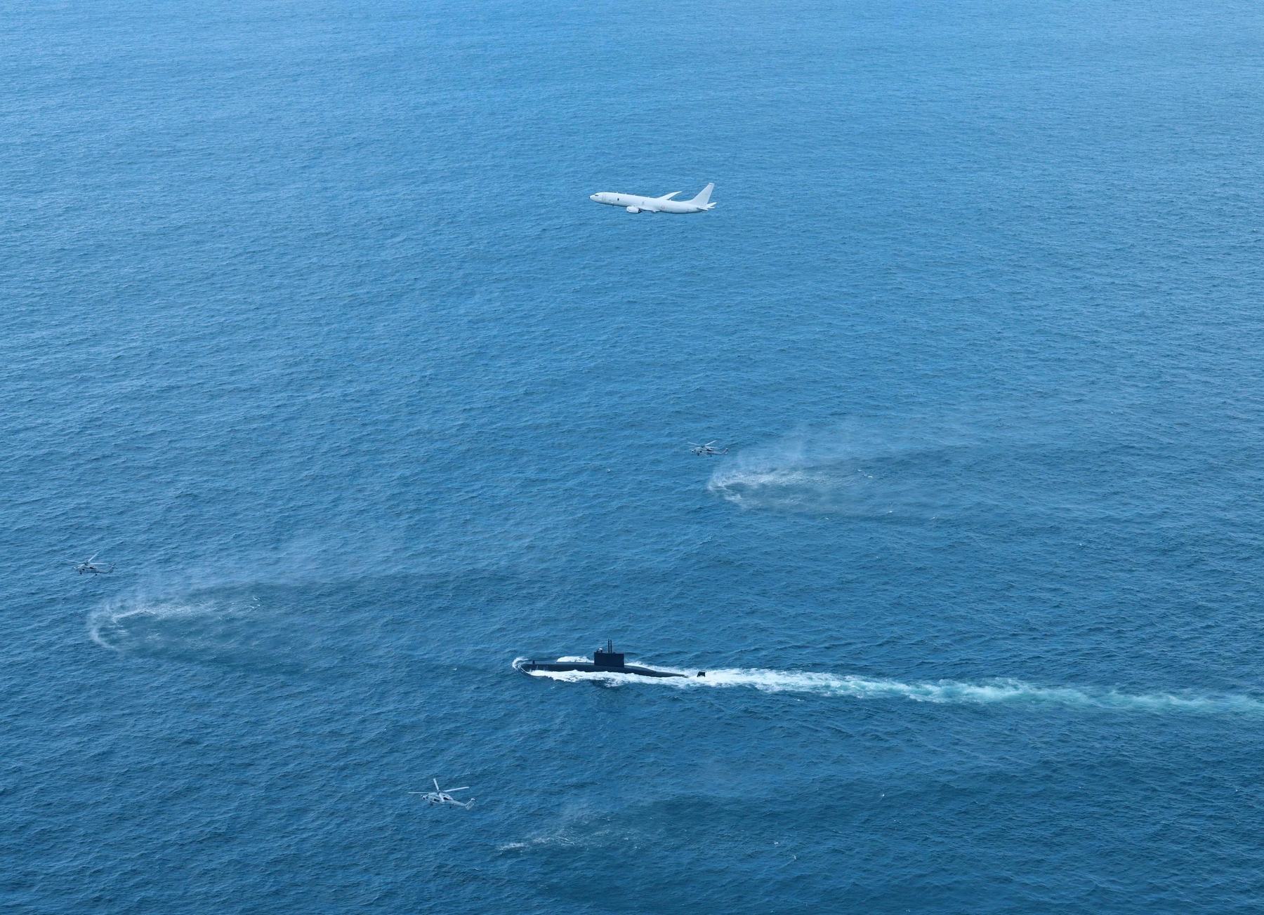 A maritime patrol aircraft and three helicopters working a surfaced submarine from the air.