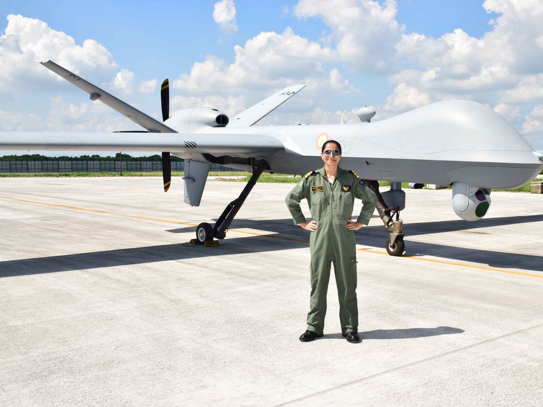 Aakriti Mehta in flying overalls on the flight line beside an MQ-9B remotely piloted aircraft.