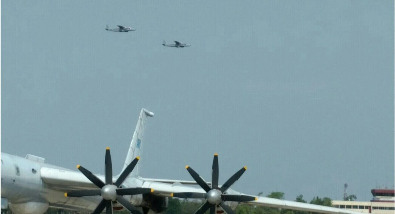 Two maritime patrol aircraft in formation over a parked long-range patrol aircraft at a naval air station.
